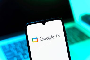 Prag, Çek Cumhuriyeti - 08 12 2025: Bir dizüstü bilgisayarın önünde duran bir cep telefonu Google TV logosunu gösteriyor. Google TV film, program ve uygulamalar için bir platformdur..
