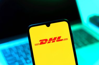 Prag, Çek Cumhuriyeti - 08 12 2025: Bilgisayarın önünde duran bir cep telefonu DHL logosunu gösteriyor. DHL uluslararası nakliye hizmeti sunan bir lojistik şirketidir..