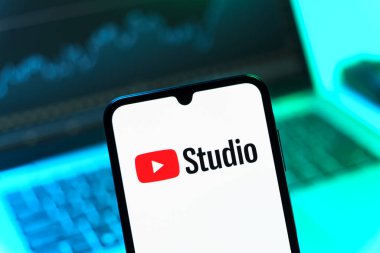 Prag, Çek Cumhuriyeti - 08 12 2025: Bir dizüstü bilgisayarın önünde duran bir cep telefonu Youtube Stüdyo logosunu gösteriyor. Youtube Studio YouTube kanallarını yönetmek ve analiz etmek için bir platformdur.