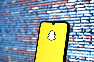 Prague, Czechia - 08 12 2025: Phone in front of a screen showing the Snapchat logo. Snapchat is an app for sending photos, videos, and temporary messages.