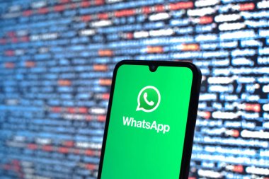 Prague, Czechia - 08 12 2025: Phone in front of a screen showing the WhatsApp logo. WhatsApp is an app for sending texts, calls, and media.