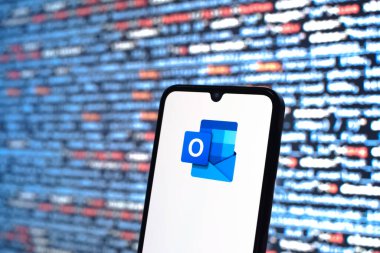 Prague, Czechia - 08 12 2025: Phone in front of a screen showing the Outlook logo. Outlook is an email platform for sending and managing messages.