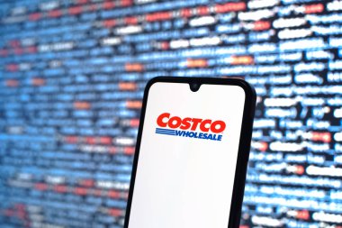 Prague, Czechia - 08 12 2025: Phone in front of a screen showing the Costco logo. Costco is a wholesale retailer selling products in bulk to members.