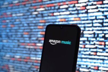 Prague, Czechia - 08 12 2025: Phone in front of a screen showing the Amazon Music logo. Amazon Music is a platform for streaming and discovering music.