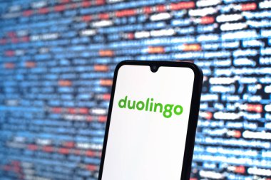 Prague, Czechia - 08 12 2025: Phone in front of a screen showing the Duolingo logo. Duolingo is a platform for learning languages interactively.