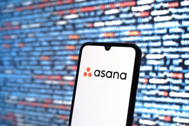Prague, Czechia - 08 12 2025: Phone in front of a screen showing the Asana logo. Asana is a platform for task management and team collaboration.