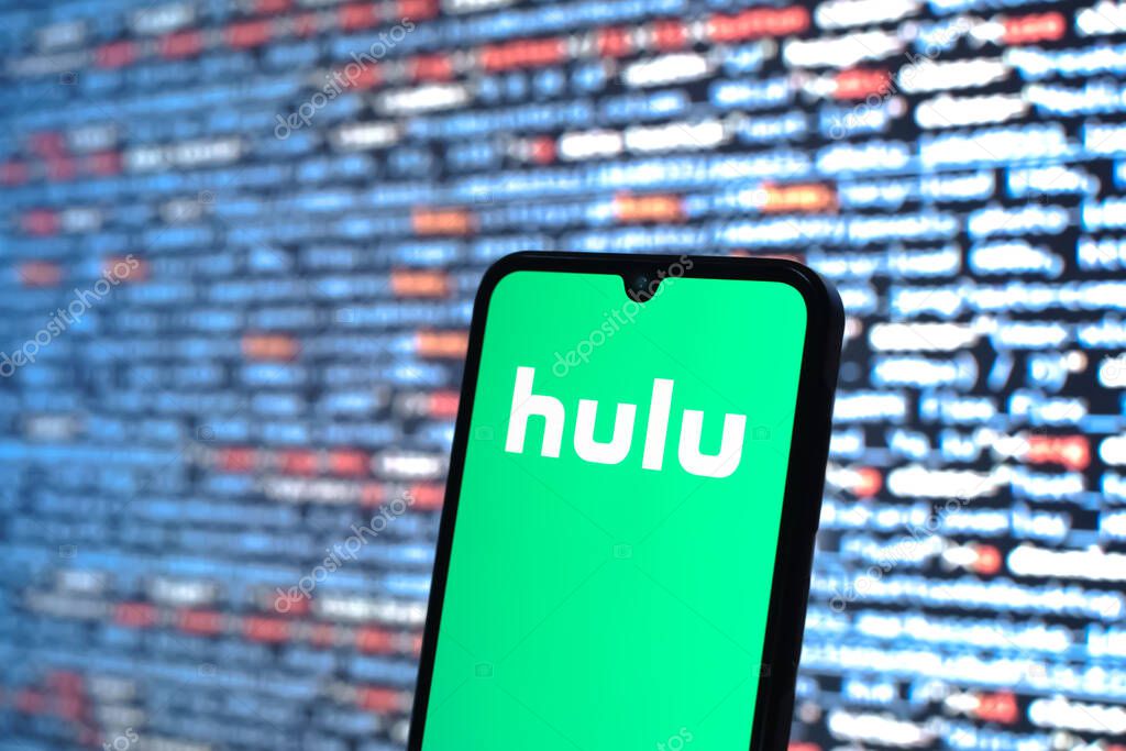 Prague, Czechia - 08 12 2025: Phone in front of a screen showing the Hulu logo. Hulu is a streaming platform for TV shows, movies, and live TV.
