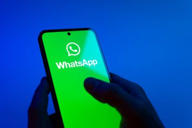 Prague, Czechia - 08 12 2025: Hands on a blue background are holding a mobile phone displaying the WhatsApp logo. WhatsApp is an app for sending texts, calls, and media.