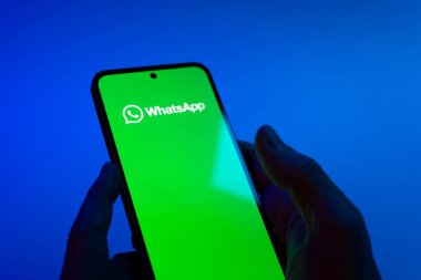 Prague, Czechia - 08 12 2025: Hands on a blue background are holding a mobile phone displaying the WhatsApp logo. WhatsApp is an app for sending texts, calls, and media.