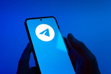 Prague, Czechia - 08 12 2025: Hands on a blue background are holding a mobile phone displaying the Telegram logo. Telegram is an app for fast and secure messaging.