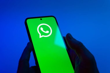 Prague, Czechia - 08 12 2025: Hands on a blue background are holding a mobile phone displaying the WhatsApp logo. WhatsApp is an app for sending texts, calls, and media.