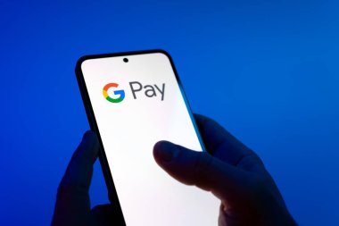 Prague, Czechia - 08 12 2025: Hands on a blue background are holding a mobile phone displaying the Google Pay logo. Google Pay is a platform for easy and secure digital payments.