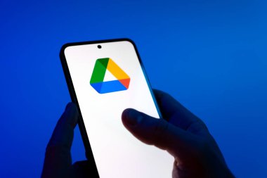 Prague, Czechia - 08 12 2025: Hands on a blue background are holding a mobile phone displaying the Google Drive logo. Google Drive is a platform for storing and sharing files online.