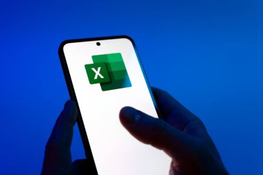 Prague, Czechia - 08 12 2025: Hands on a blue background are holding a mobile phone displaying the Excel logo. Excel is a software for spreadsheets, data analysis, and calculations.