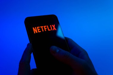 Prag, Çek Cumhuriyeti - 08 12 2025: Mavi arkaplandaki eller Netflix logosunu gösteren bir cep telefonu tutuyor. Netflix sinema ve televizyon programları için bir yayın platformudur..