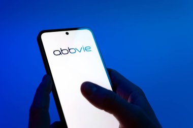 Prag, Çek Cumhuriyeti - 08 12 2025: Mavi arkaplandaki eller AbbVie logosunu gösteren bir cep telefonu tutuyor. AbbVie ilaç ve terapi geliştiren bir biyofarmasötik şirketidir..