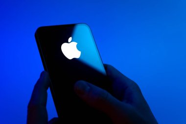 Prag, Çek Cumhuriyeti - 08 12 2025: Mavi arkaplandaki eller Apple logosunu gösteren bir cep telefonu tutuyor. Apple iPhone, bilgisayar ve hizmet üreten bir teknoloji şirketidir..