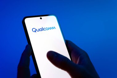Prag, Çek Cumhuriyeti - 08 12 2025: Mavi arkaplandaki eller Qualcomm logosunu gösteren bir cep telefonu tutuyor. Qualcomm, mobil çipler ve modemler üzerine uzmanlaşmış bir yarı iletken şirketidir..