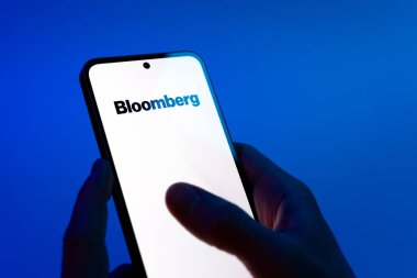 Prag, Çek Cumhuriyeti - 08 12 2025: Mavi arkaplandaki eller Bloomberg logosunu gösteren bir cep telefonu tutuyor. Bloomberg finansal haberler, veriler ve analizler sağlayan bir şirkettir..