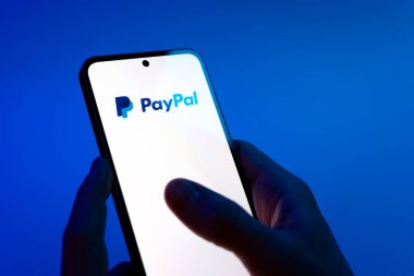 Prag, Çek Cumhuriyeti - 08 12 2025: Mavi arkaplandaki eller PayPal logosunu gösteren bir cep telefonu tutuyor. PayPal çevrimiçi ödemeler ve para transferleri için bir platformdur.