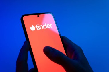 Prag, Çek Cumhuriyeti - 08 12 2025: Mavi arkaplandaki eller Tinder logosunu gösteren bir cep telefonu tutuyor. Tinder insanları eşleştirmek ve bağlamak için bir randevu uygulaması.