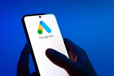 Prag, Çek Cumhuriyeti - 08 12 2025: Mavi arkaplandaki eller Google Ads logosunu gösteren bir cep telefonu tutuyor. Google Reklamları, çevrimiçi reklamlar yaratmak ve yönetmek için bir platformdur.