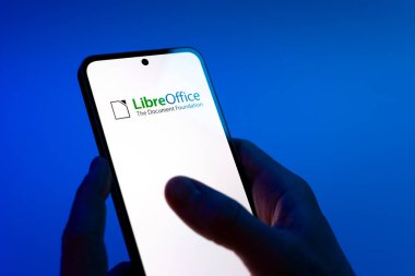 Prag, Çek Cumhuriyeti - 08 12 2025: Eller mavi arkaplanda LibreOffice logosunu gösteren bir cep telefonu tutuyor. LibreOffice, dokümanlar, hesap tabloları ve sunumlar oluşturmak için özgür bir yazılım takımıdır..