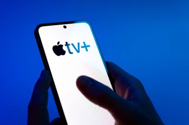 Prag, Çek Cumhuriyeti - 08 12 2025: Mavi arkaplandaki eller Apple TV + logosunu gösteren bir cep telefonu tutuyor. Apple TV +, filmler ve TV programları için bir yayın platformudur..