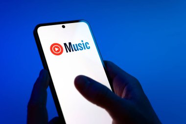 Prag, Çek Cumhuriyeti - 08 12 2025: Eller mavi arkaplanda Youtube Müzik logosunu gösteren bir cep telefonu tutuyor. Youtube Music müzik için bir platformdur..