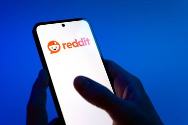 Prag, Çek Cumhuriyeti - 08 12 2025: Mavi arkaplandaki eller Reddit logosunu gösteren bir cep telefonu tutuyor. Reddit tartışma, haber ve toplum içeriği için bir platformdur.