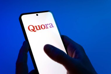 Prag, Çek Cumhuriyeti - 08 12 2025: Mavi arkaplandaki eller Quora logosunu gösteren bir cep telefonu tutuyor. Quora soru sormak ve bilgi paylaşmak için bir platformdur..