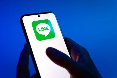 Prag, Çek Cumhuriyeti - 08 12 2025: Mavi arkaplandaki eller hat logosunu gösteren bir cep telefonu tutuyor. Line aramalar, mesajlar ve çokluortam paylaşımı için bir mesajlaşma uygulamasıdır.