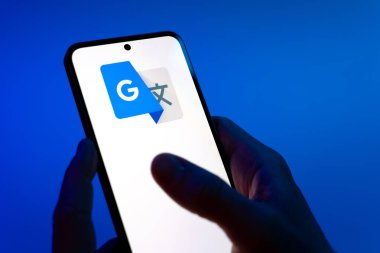 Prag, Çek Cumhuriyeti - 08 12 2025: Mavi arkaplandaki eller Google Translate logosunu gösteren bir cep telefonu tutuyor. Google Çevirisi metni ve konuşmayı diller arası çevirmek için bir platformdur..