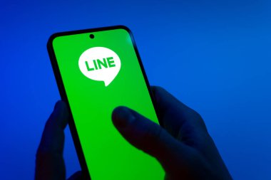 Prag, Çek Cumhuriyeti - 08 12 2025: Mavi arkaplandaki eller hat logosunu gösteren bir cep telefonu tutuyor. Line aramalar, mesajlar ve çokluortam paylaşımı için bir mesajlaşma uygulamasıdır.