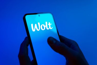 Prag, Çek Cumhuriyeti - 08 12 2025: Mavi arkaplandaki eller Wolt logosunu gösteren bir cep telefonu tutuyor. Wolt yemek ve teslimat hizmetleri için bir platformdur..