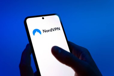 Prag, Çek Cumhuriyeti - 08 12 2025: Mavi arkaplandaki eller NordVPN logosunu gösteren bir cep telefonu tutuyor. NordVPN güvenli ve özel internet taraması için bir platformdur.