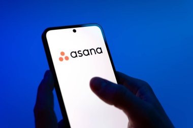 Prag, Çek Cumhuriyeti - 08 12 2025: Mavi arkaplandaki eller Asana logosunu gösteren bir cep telefonu tutuyor. Asana görev yönetimi ve takım işbirliği için bir platformdur..