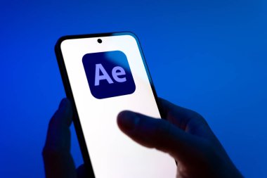 Prag, Çek Cumhuriyeti - 08 12 2025: Mavi arkaplandaki eller After Effects logosunu gösteren bir cep telefonu tutuyor. After Effects hareket grafikleri ve görsel efektler için bir yazılımdır..