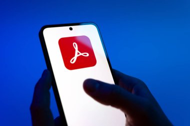Prag, Çek Cumhuriyeti - 08 12 2025: Mavi arkaplandaki eller Acrobat Reader logosunu gösteren bir cep telefonu tutuyor. Acrobat Reader, PDF belgelerini görüntülemek ve yönetmek için bir platformdur.