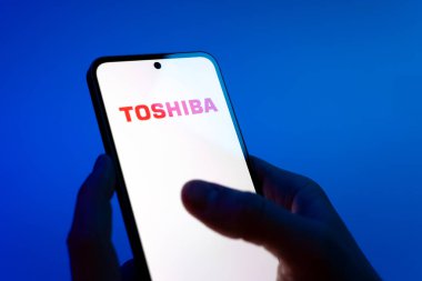 Prag, Çek Cumhuriyeti - 08 12 2025: Eller mavi arkaplanda Toshiba logosunu gösteren bir cep telefonu tutuyor. Toshiba elektronik ve cihaz üreten bir teknoloji şirketidir..