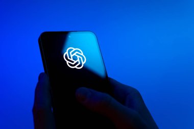 Prag, Çek Cumhuriyeti - 08 12 2025: Eller mavi arkaplanda OpenAI logosunu gösteren bir cep telefonu tutuyor. OpenAI, yapay zeka modelleri ve uygulamaları geliştiren bir platformdur..