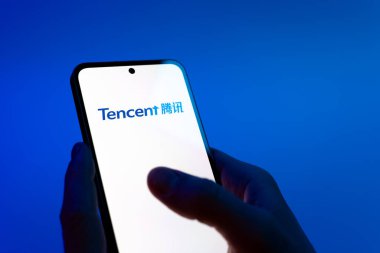 Prag, Çek Cumhuriyeti - 08 12 2025: Mavi arkaplandaki eller Tencent logosunu gösteren bir cep telefonu tutuyor. Tencent internet hizmetleri ve oyunlar sağlayan bir teknoloji şirketidir..