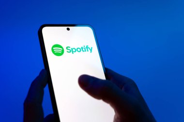 Prag, Çek Cumhuriyeti - 08 12 2025: Mavi arkaplandaki eller Spotify logosunu gösteren bir cep telefonu tutuyor. Spotify müzik dinlemek ve keşfetmek için bir platformdur.
