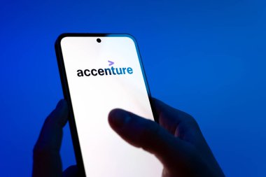 Prague, Czechia - 08 12 2025: Hands on a blue background are holding a mobile phone displaying the Accenture logo. Accenture is a consulting and professional services company.