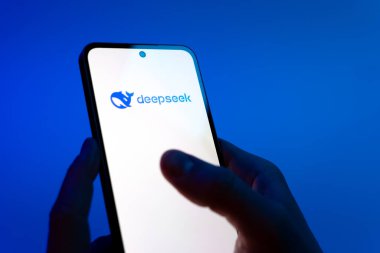 Prag, Çek Cumhuriyeti - 08 12 2025: Mavi arkaplandaki eller Deepseek logosunu gösteren bir cep telefonu tutuyor. Deepseek yapay zeka destekli arama ve araştırma için bir platformdur.