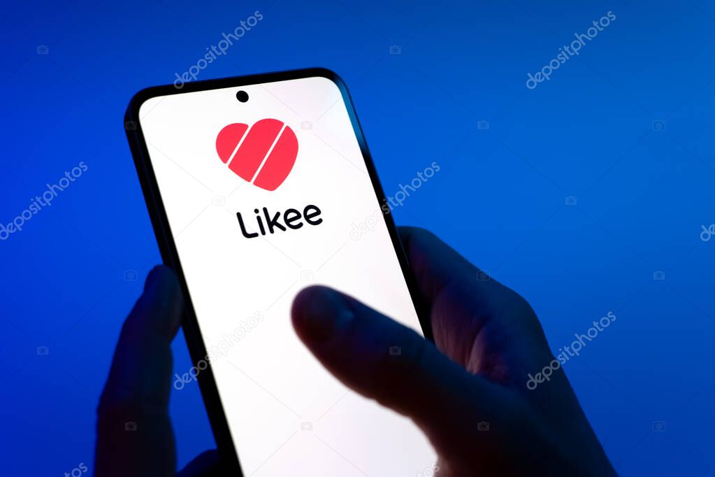 Prague, Czechia - 08 12 2025: Hands on a blue background are holding a mobile phone displaying the Likee logo. Likee is a platform for creating and sharing short videos.