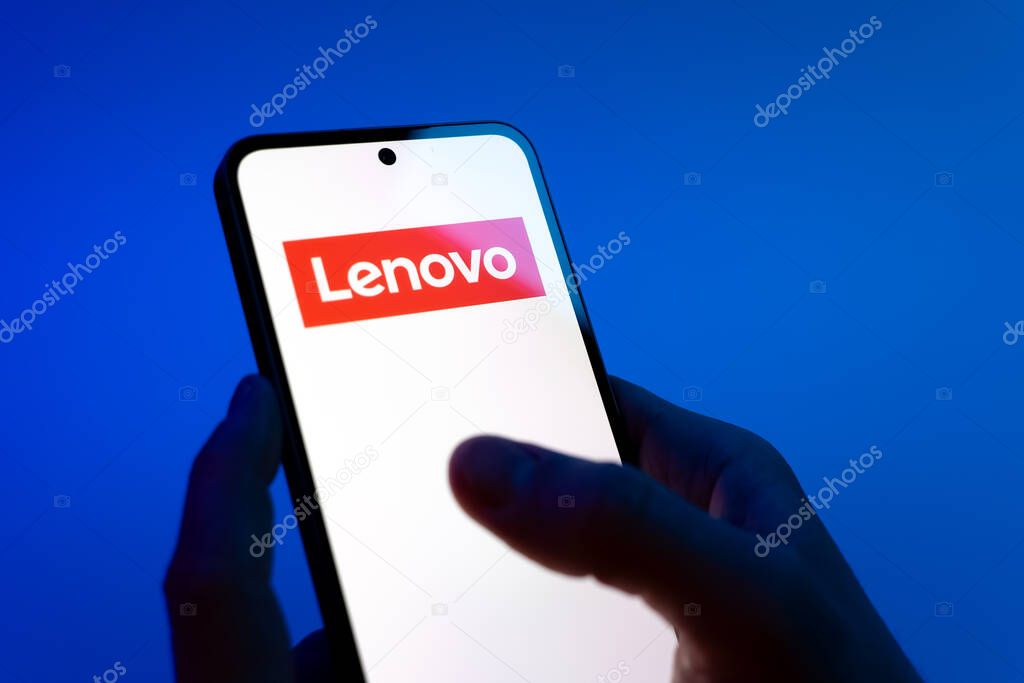 Prague, Czechia - 08 12 2025: Hands on a blue background are holding a mobile phone displaying the Lenovo logo. Lenovo is a technology company producing computers and electronics.