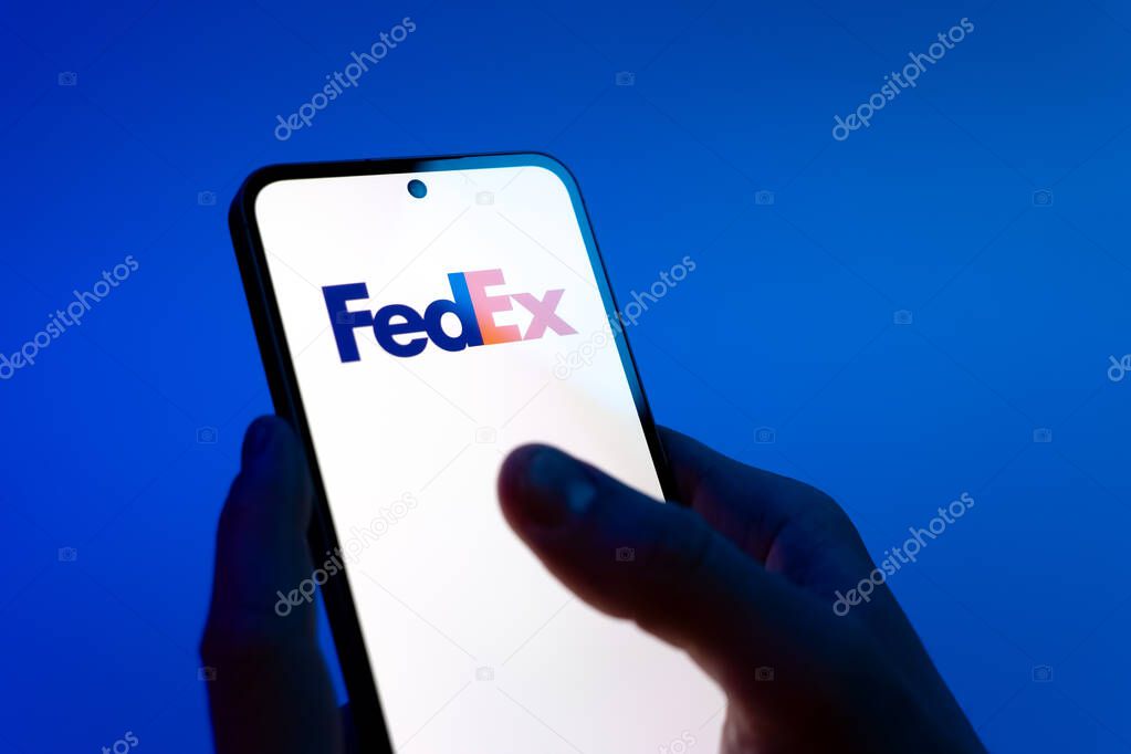 Prague, Czechia - 08 12 2025: Hands on a blue background are holding a mobile phone displaying the FedEX logo. FedEX is a logistics company providing shipping and courier services.
