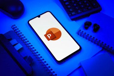 Prag, Çek Cumhuriyeti - 08 18 2025: Merkezde Powerpoint logosunu gösteren bir cep telefonu ile ofis malzemeleri düzenlemesi. Powerpoint sunumlar ve slayt gösterileri oluşturmak için bir yazılımdır..