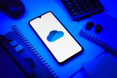 Prag, Çek Cumhuriyeti - 08 18 2025: Merkezde OneDrive logosunu gösteren bir cep telefonu ile ofis malzemeleri düzenlemesi. OneDrive dosyaları kaydetmek ve paylaşmak için bir bulut depolama platformudur.